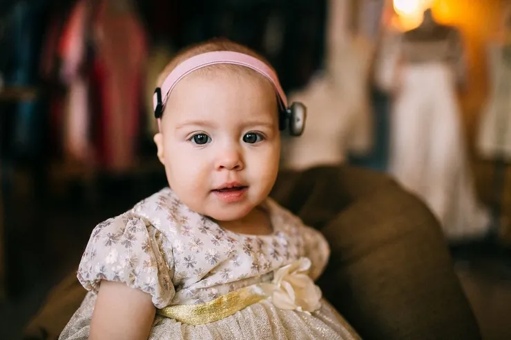 Baby girl in beautiful dress with matching hearing device