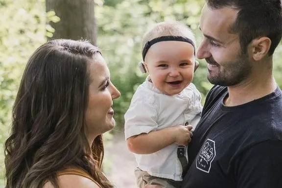 Smiling baby wearing a hearing device with their parents